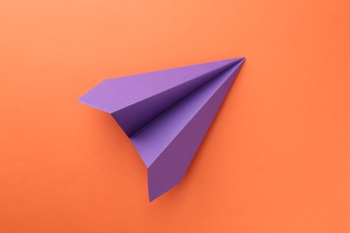 Photo of One handmade violet paper plane on orange background, top view