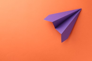 Photo of One handmade violet paper plane on orange background, top view. Space for text