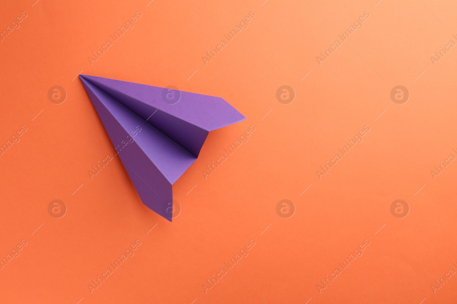 Photo of One handmade violet paper plane on orange background, top view. Space for text