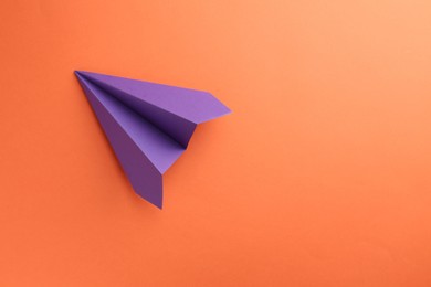 Photo of One handmade violet paper plane on orange background, top view. Space for text