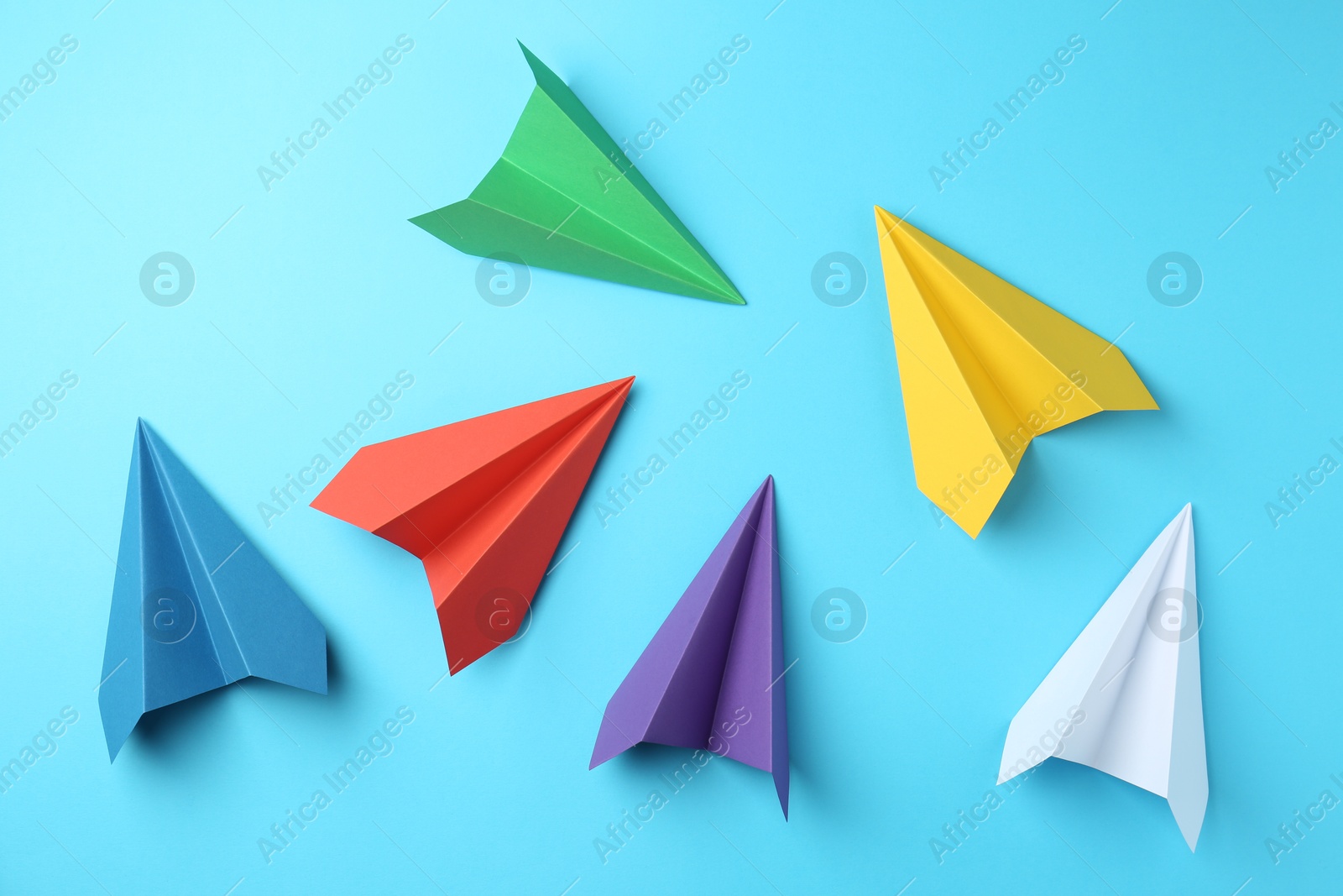 Photo of Handmade color paper planes on light blue background, flat lay