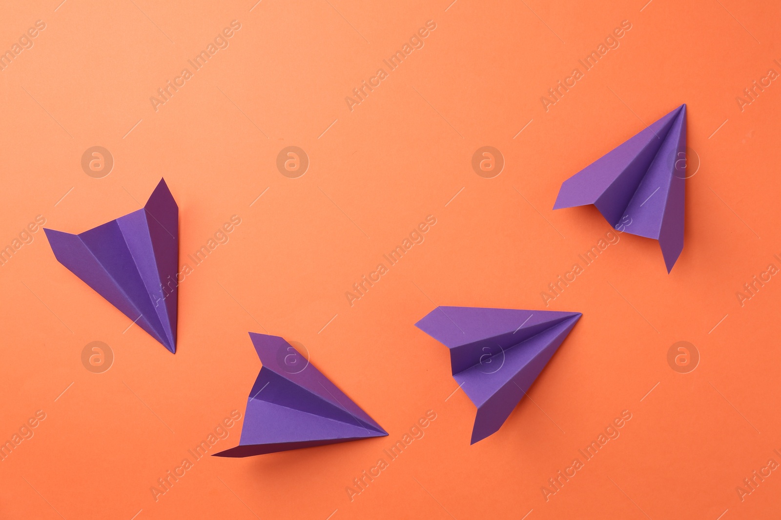 Photo of Handmade purple paper planes on orange background, top view