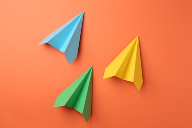 Photo of Handmade color paper planes on orange background, flat lay