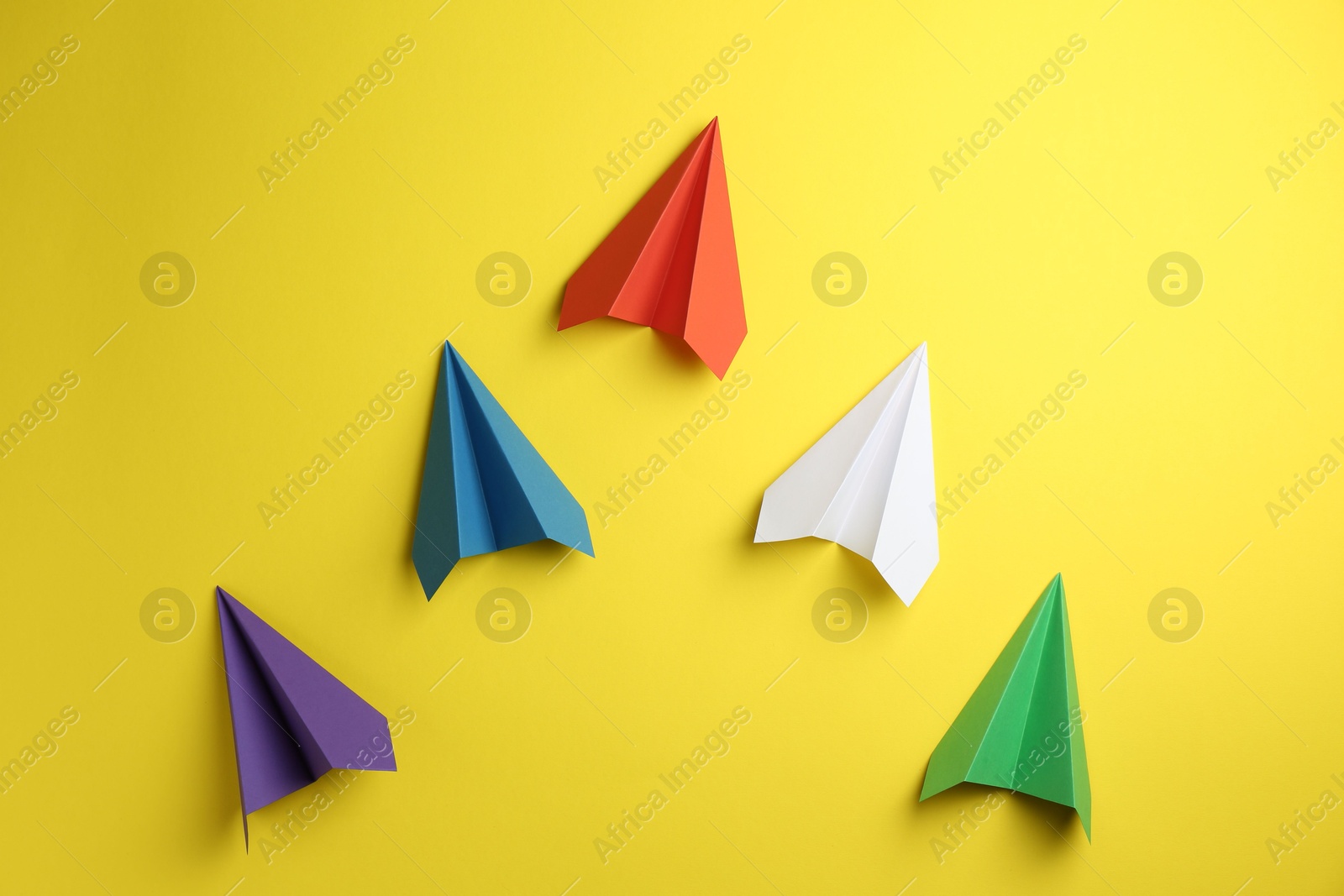 Photo of Handmade color paper planes on yellow background, flat lay