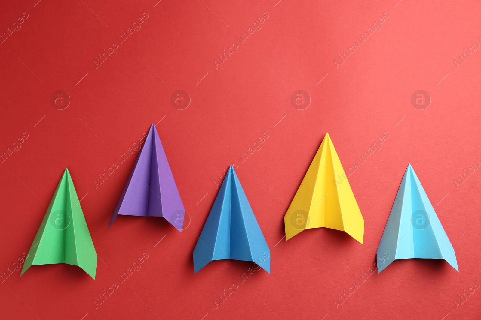 Photo of Colorful paper planes on red background, top view