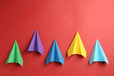 Photo of Colorful paper planes on red background, top view