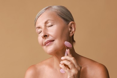 Beautiful woman doing facial massage with roller on beige background