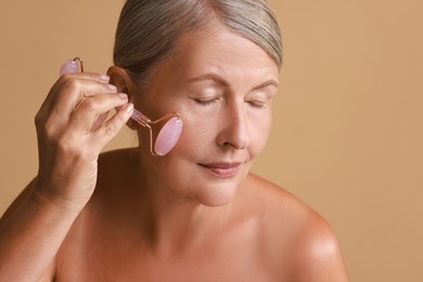 Photo of Beautiful woman doing facial massage with roller on beige background