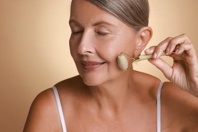 Photo of Beautiful woman doing facial massage with roller on beige background