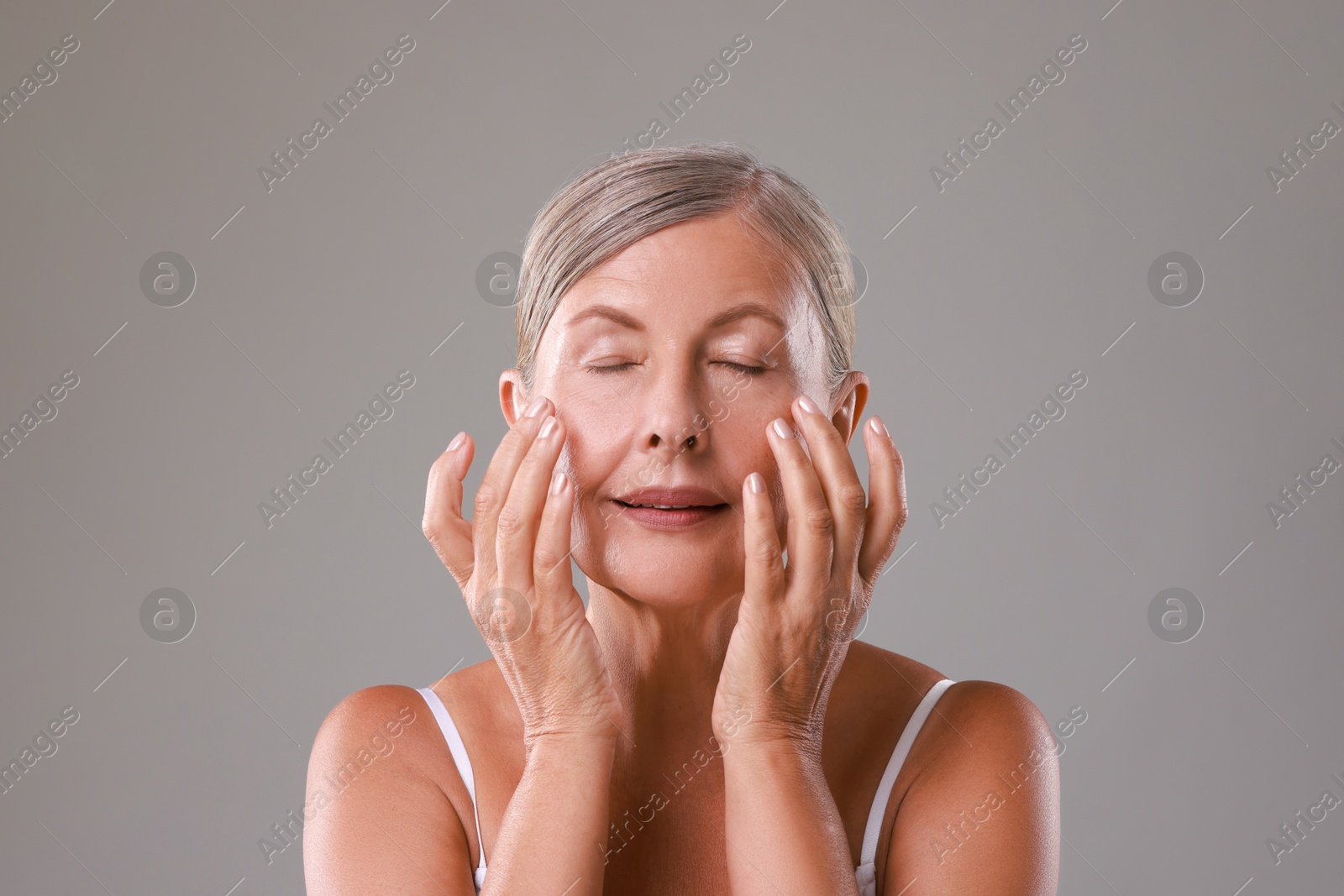 Photo of Beautiful woman doing facial massage on grey background