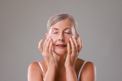 Photo of Beautiful woman doing facial massage on grey background