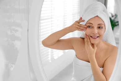 Photo of Smiling woman doing facial self massage near mirror in bathroom