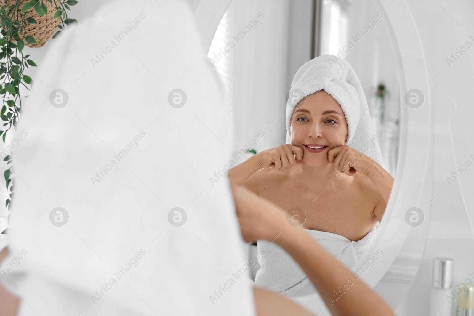 Photo of Smiling woman doing facial self massage near mirror in bathroom