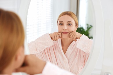 Photo of Beautiful woman doing facial self massage near mirror in bathroom