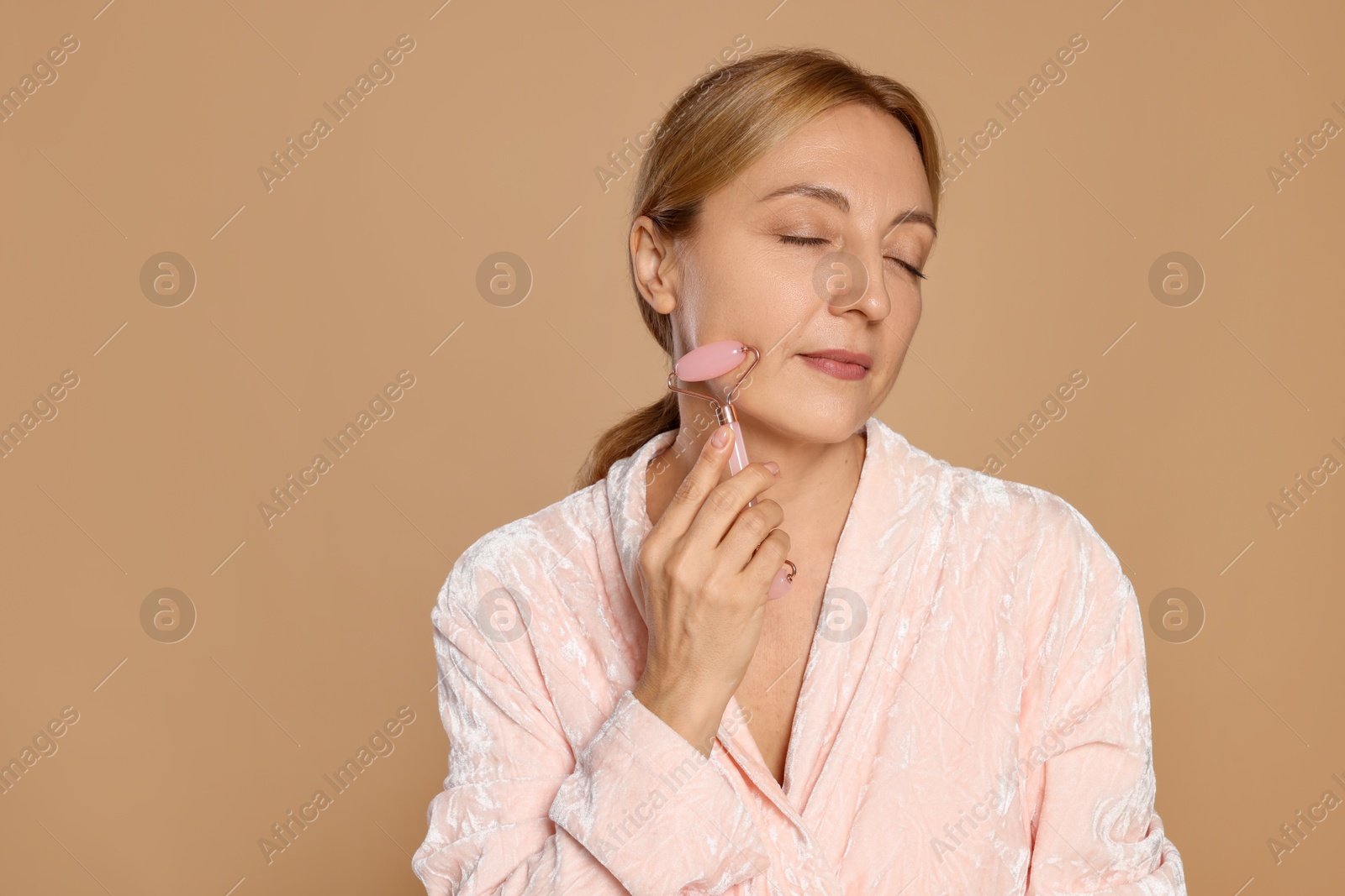 Photo of Beautiful woman doing facial self massage with roller on beige background. Space for text