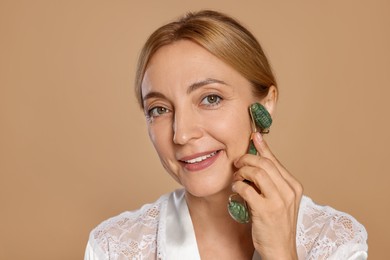 Smiling woman doing facial self massage with roller on beige background