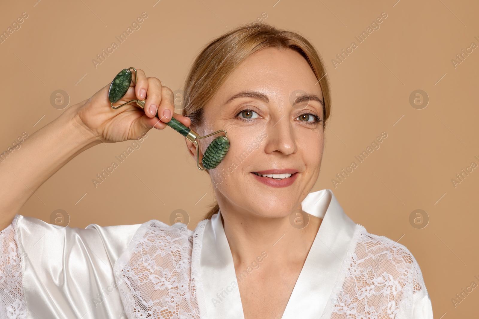 Photo of Smiling woman doing facial self massage with roller on beige background