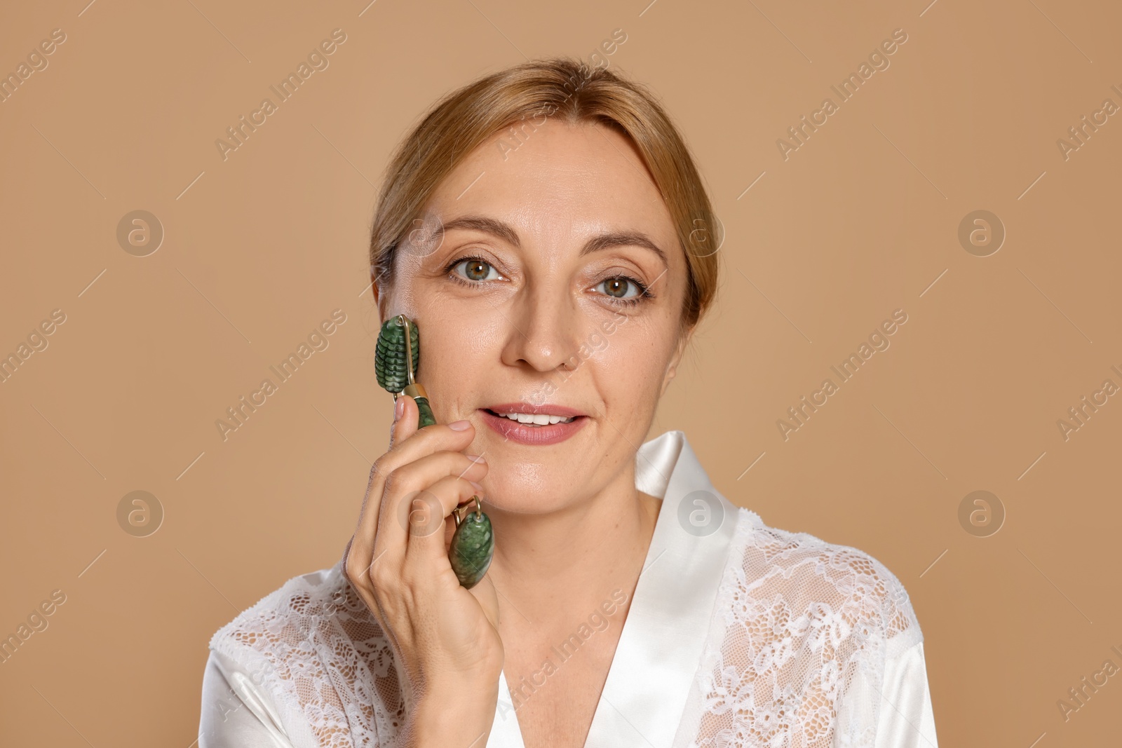 Photo of Smiling woman doing facial self massage with roller on beige background