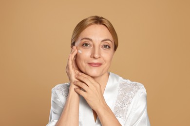 Beautiful woman with cream on face against beige background