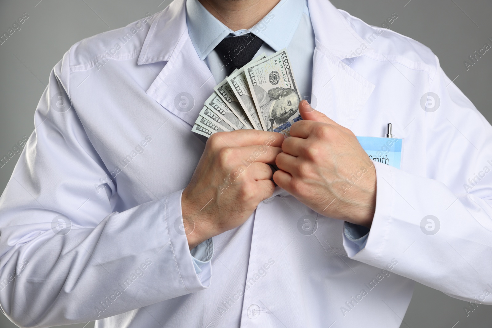 Photo of Corruption concept. Doctor putting dollar banknotes into his coat on grey background, closeup