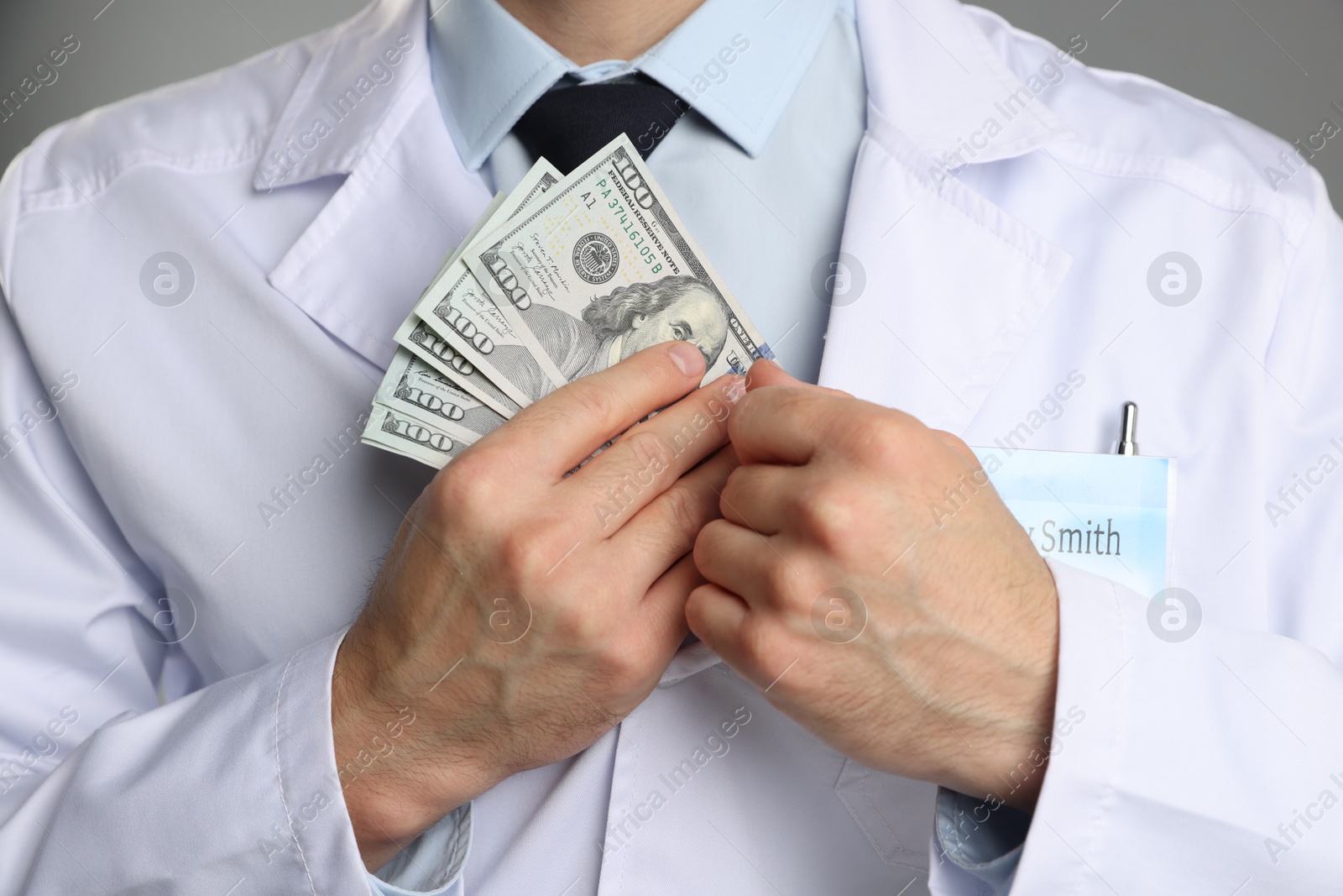 Photo of Corruption concept. Doctor putting dollar banknotes into his coat on grey background, closeup