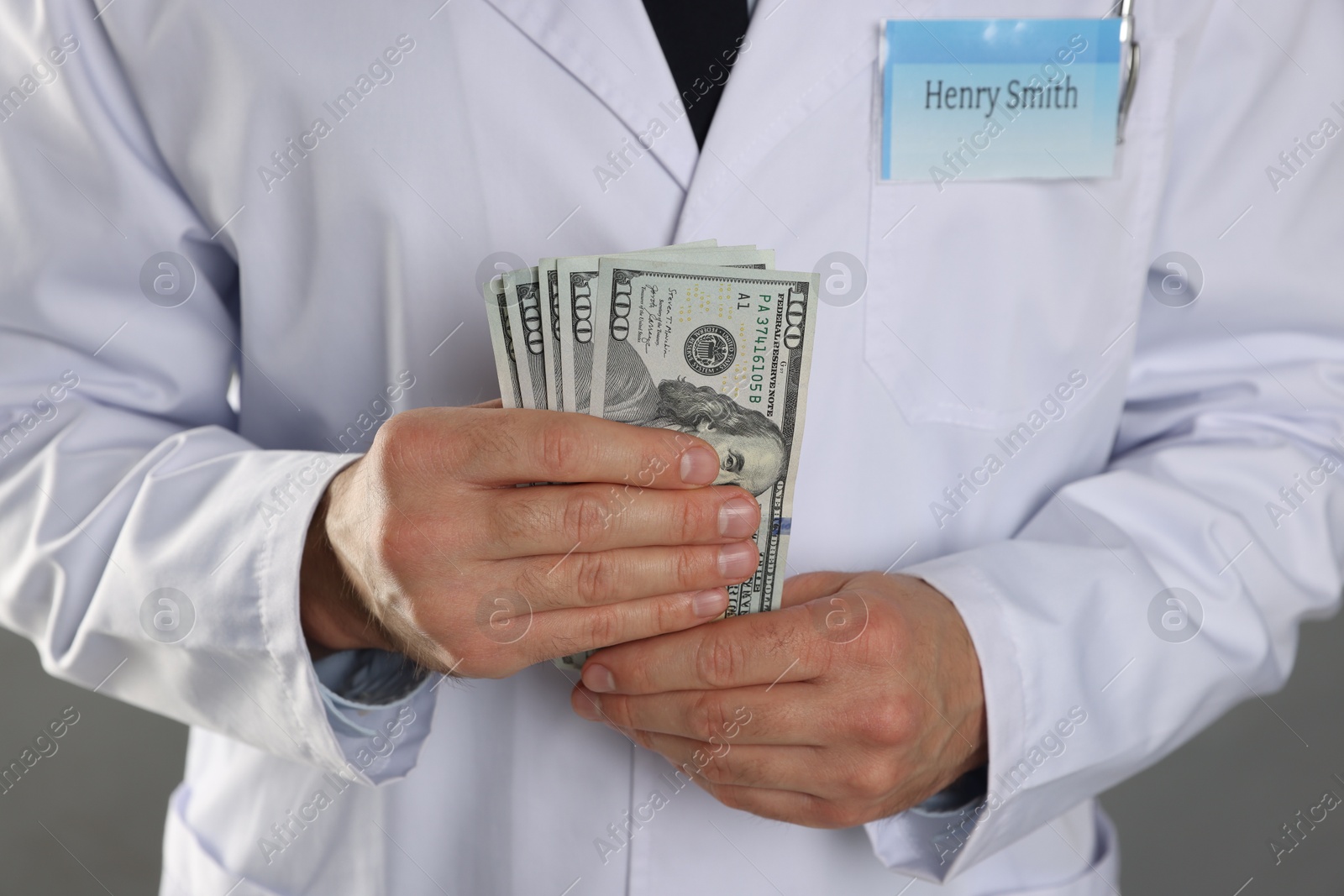 Photo of Corruption concept. Doctor with dollar banknotes on grey background, closeup