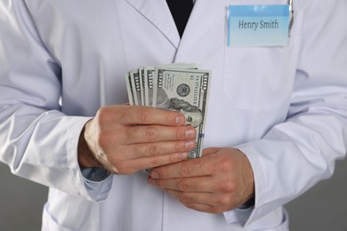 Photo of Corruption concept. Doctor with dollar banknotes on grey background, closeup