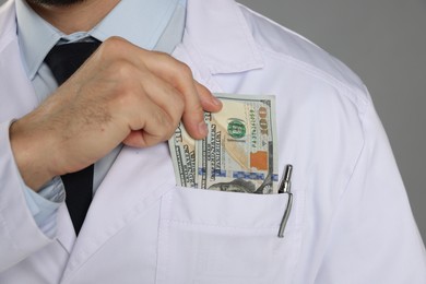 Photo of Corruption concept. Doctor putting dollar banknotes into his pocket on grey background, closeup