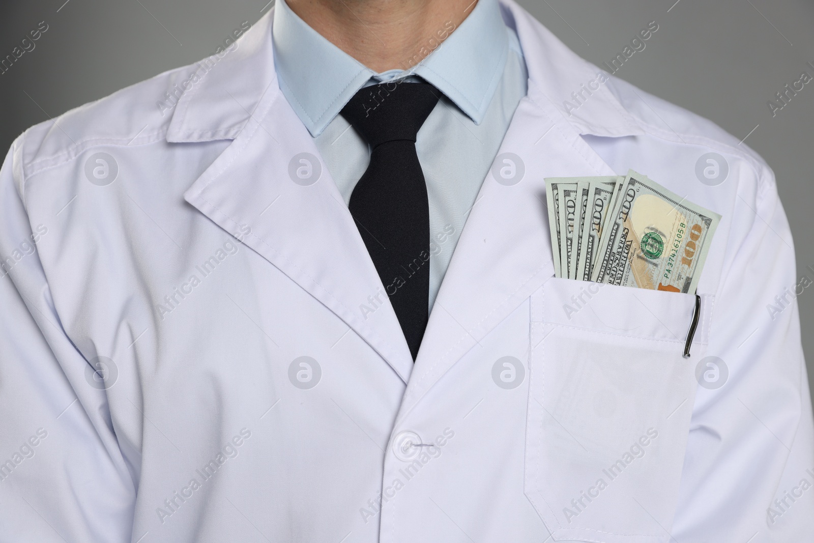 Photo of Corruption concept. Doctor with dollar banknotes on grey background, closeup