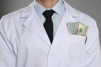 Photo of Corruption concept. Doctor with dollar banknotes on grey background, closeup