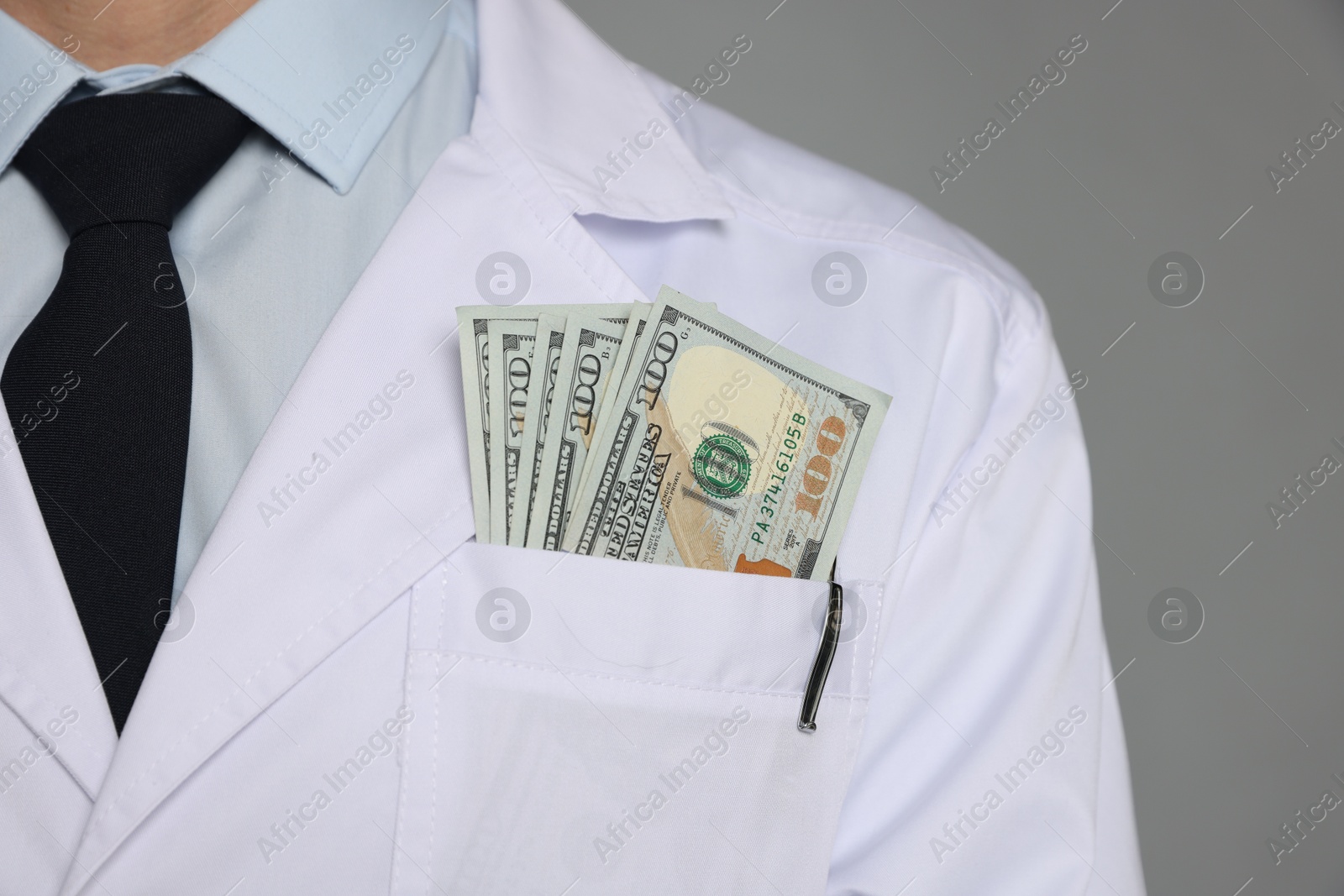 Photo of Corruption concept. Doctor with dollar banknotes on grey background, closeup