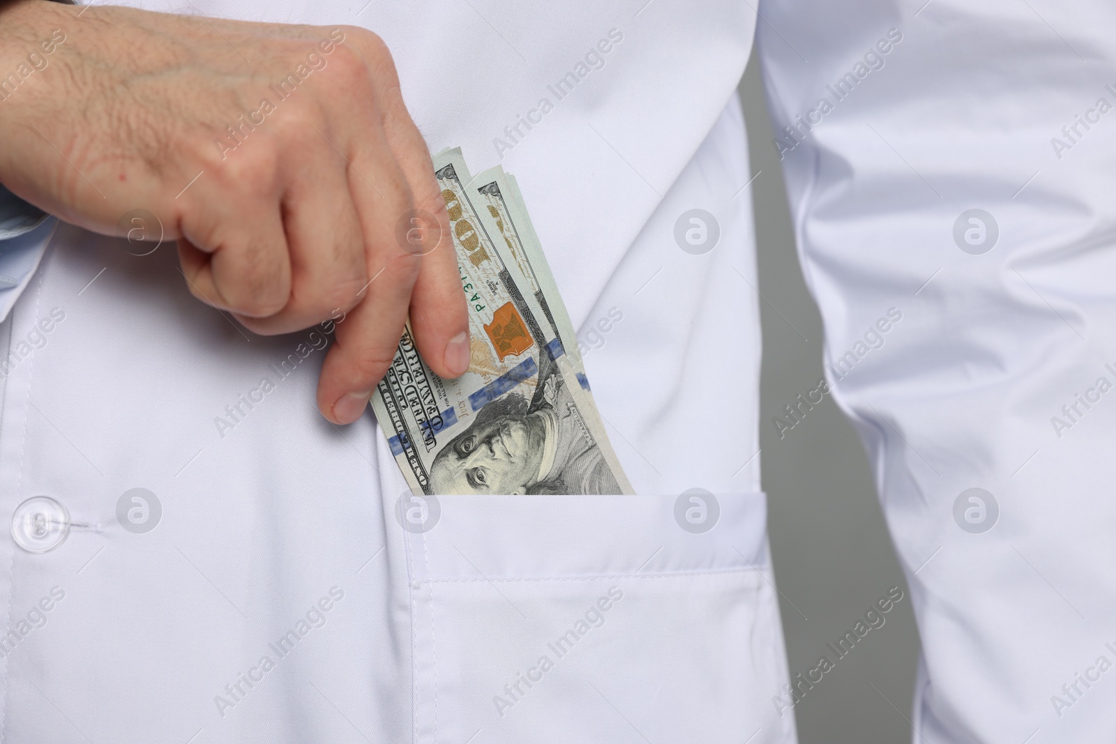 Photo of Corruption concept. Doctor putting dollar banknotes into his pocket on grey background, closeup