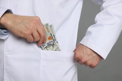 Photo of Corruption concept. Doctor putting dollar banknotes into his pocket on grey background, closeup