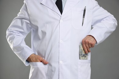 Photo of Corruption concept. Doctor putting dollar banknotes into his pocket on grey background, closeup