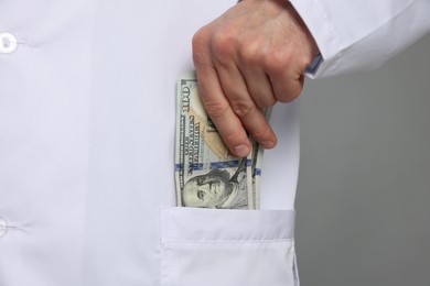 Photo of Corruption concept. Doctor putting dollar banknotes into his pocket on grey background, closeup