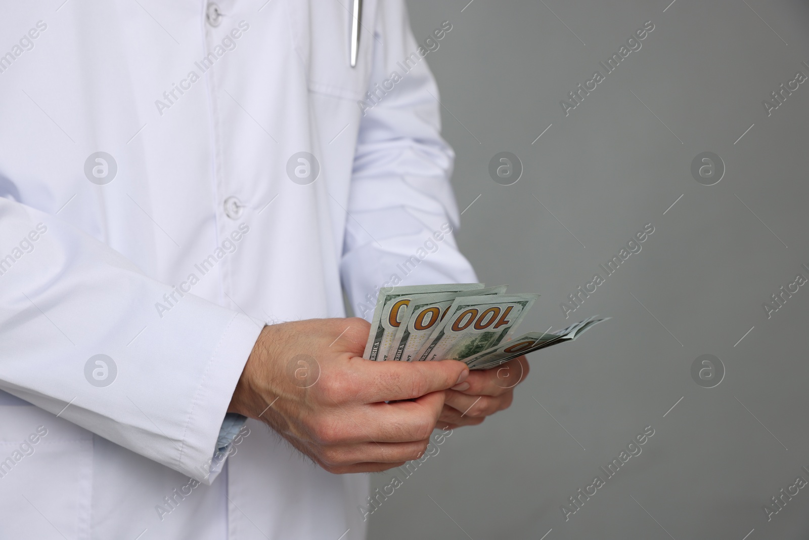 Photo of Corruption concept. Doctor with dollar banknotes on grey background, closeup. Space for text