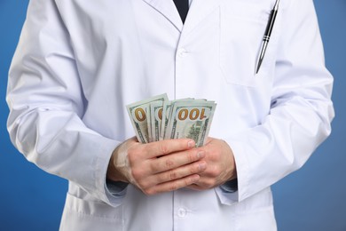 Photo of Corruption concept. Doctor with dollar banknotes on blue background, closeup