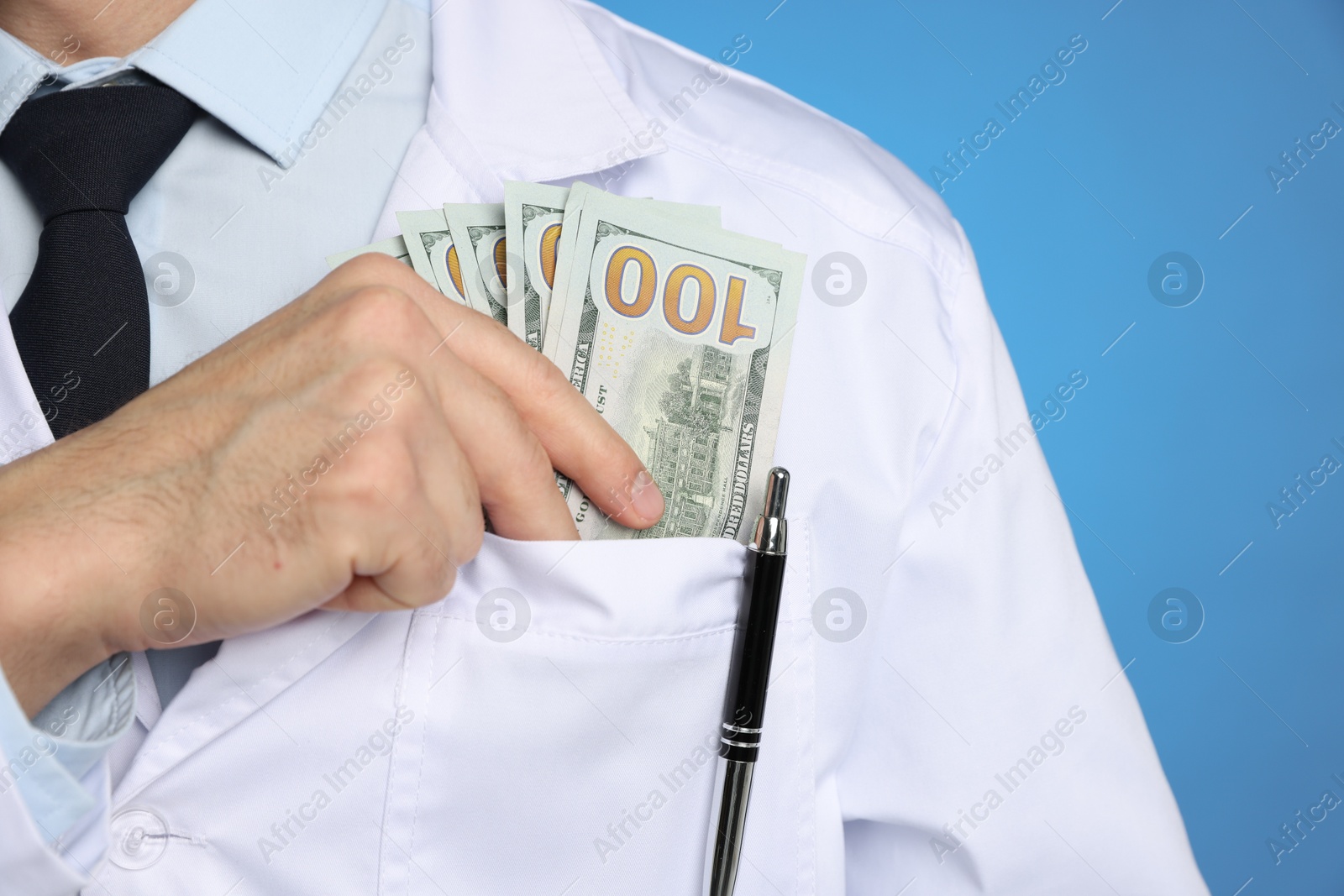 Photo of Corruption concept. Doctor putting dollar banknotes into his pocket on blue background, closeup