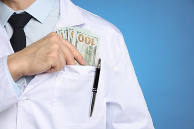 Photo of Corruption concept. Doctor putting dollar banknotes into his pocket on blue background, closeup