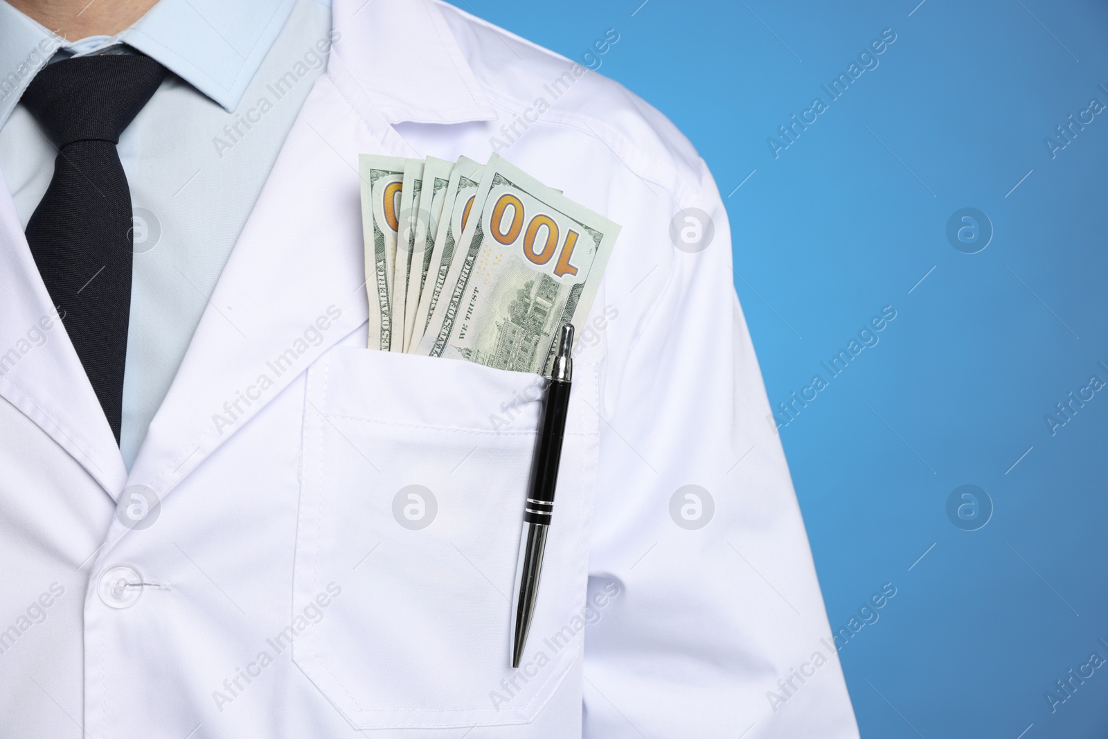 Photo of Corruption concept. Doctor with dollar banknotes on blue background, closeup