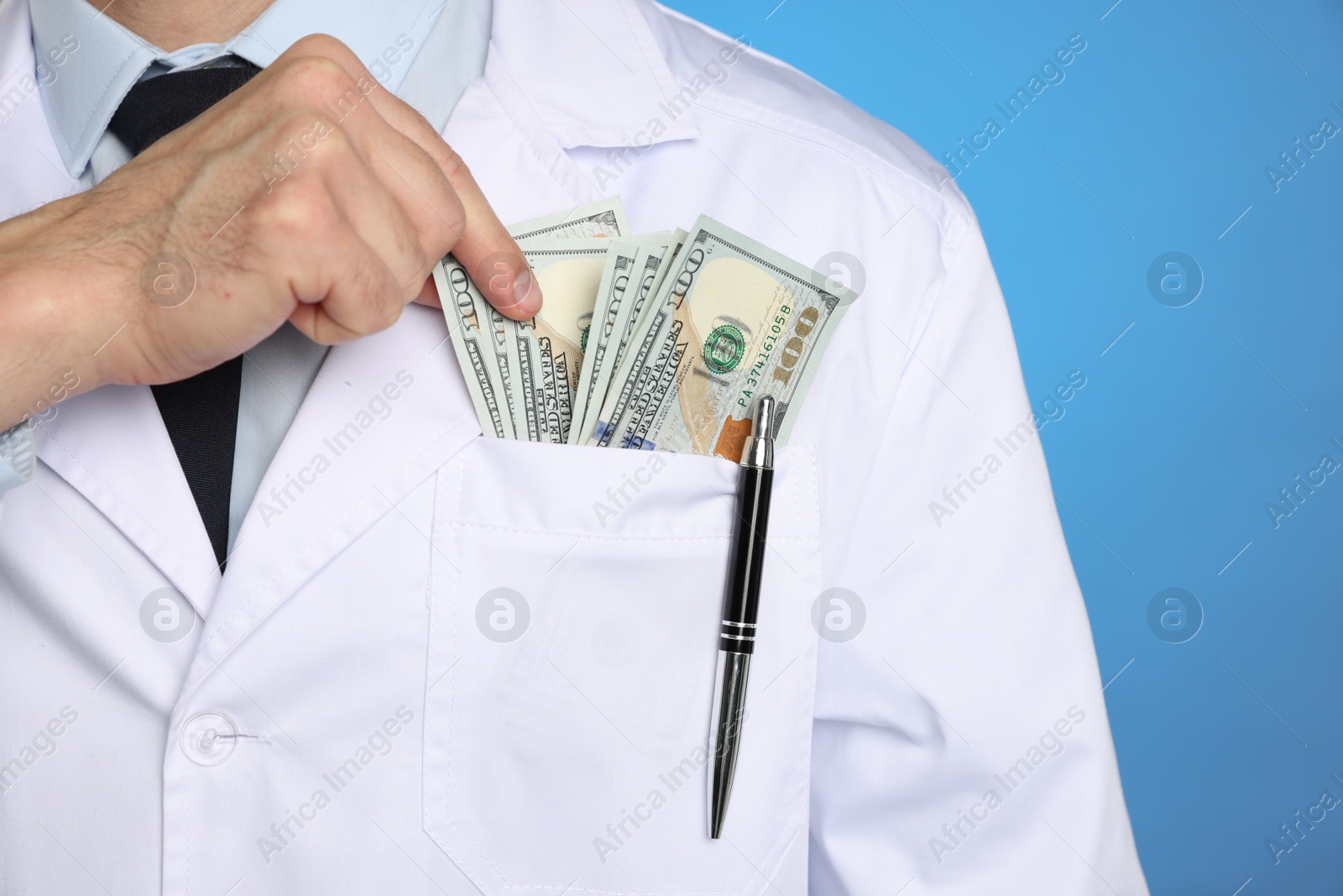 Photo of Corruption concept. Doctor putting dollar banknotes into his pocket on blue background, closeup