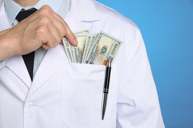 Photo of Corruption concept. Doctor putting dollar banknotes into his pocket on blue background, closeup