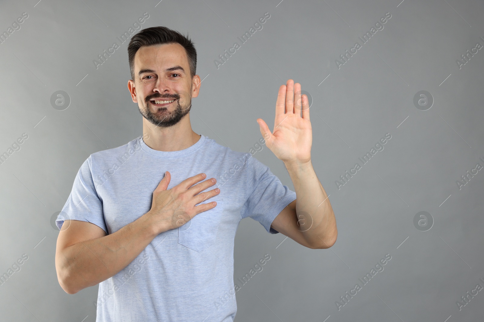 Photo of Man making promise with raised hand on grey background, space for text. Oath gesture