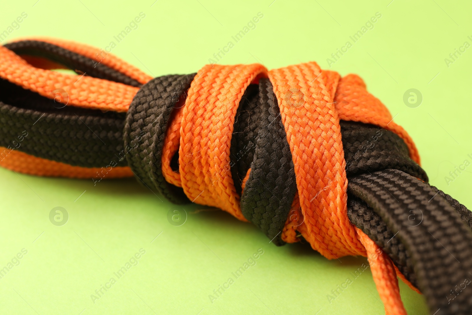 Photo of Shoelaces tied in knot on light green background, closeup. Unity concept