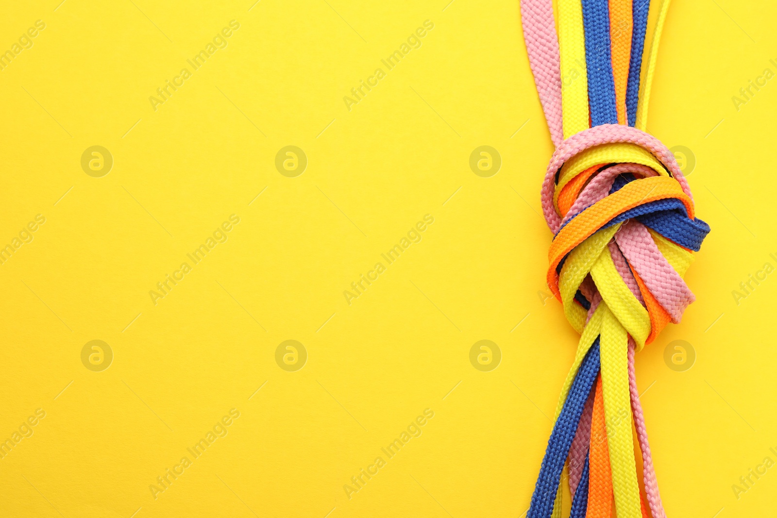 Photo of Colorful shoelaces tied in knot on yellow background, top view with space for text. Unity concept