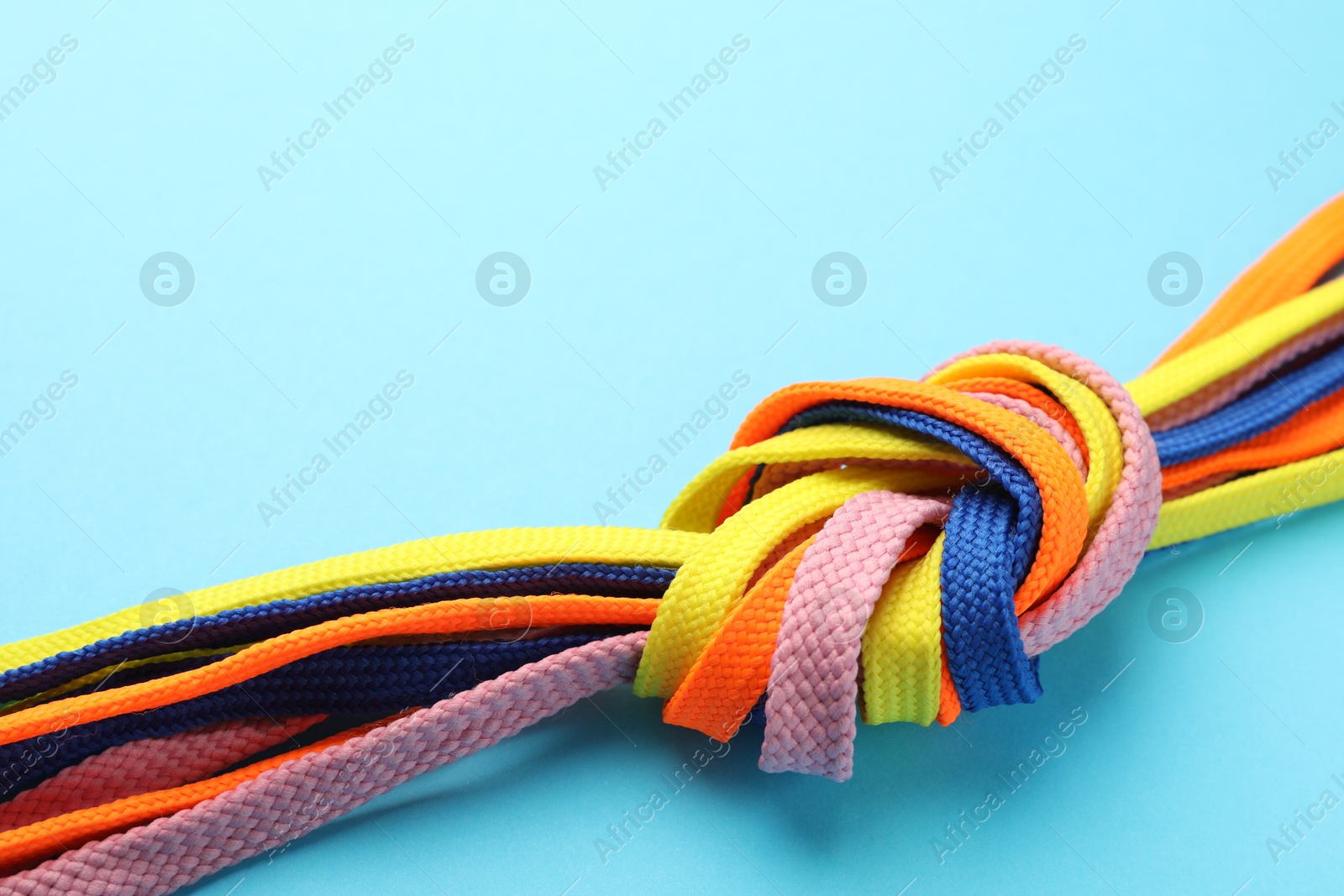 Photo of Colorful shoelaces tied in knot on light blue background, closeup. Unity concept