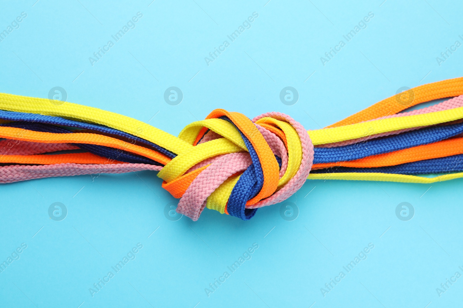 Photo of Colorful shoelaces tied in knot on light blue background, top view. Unity concept