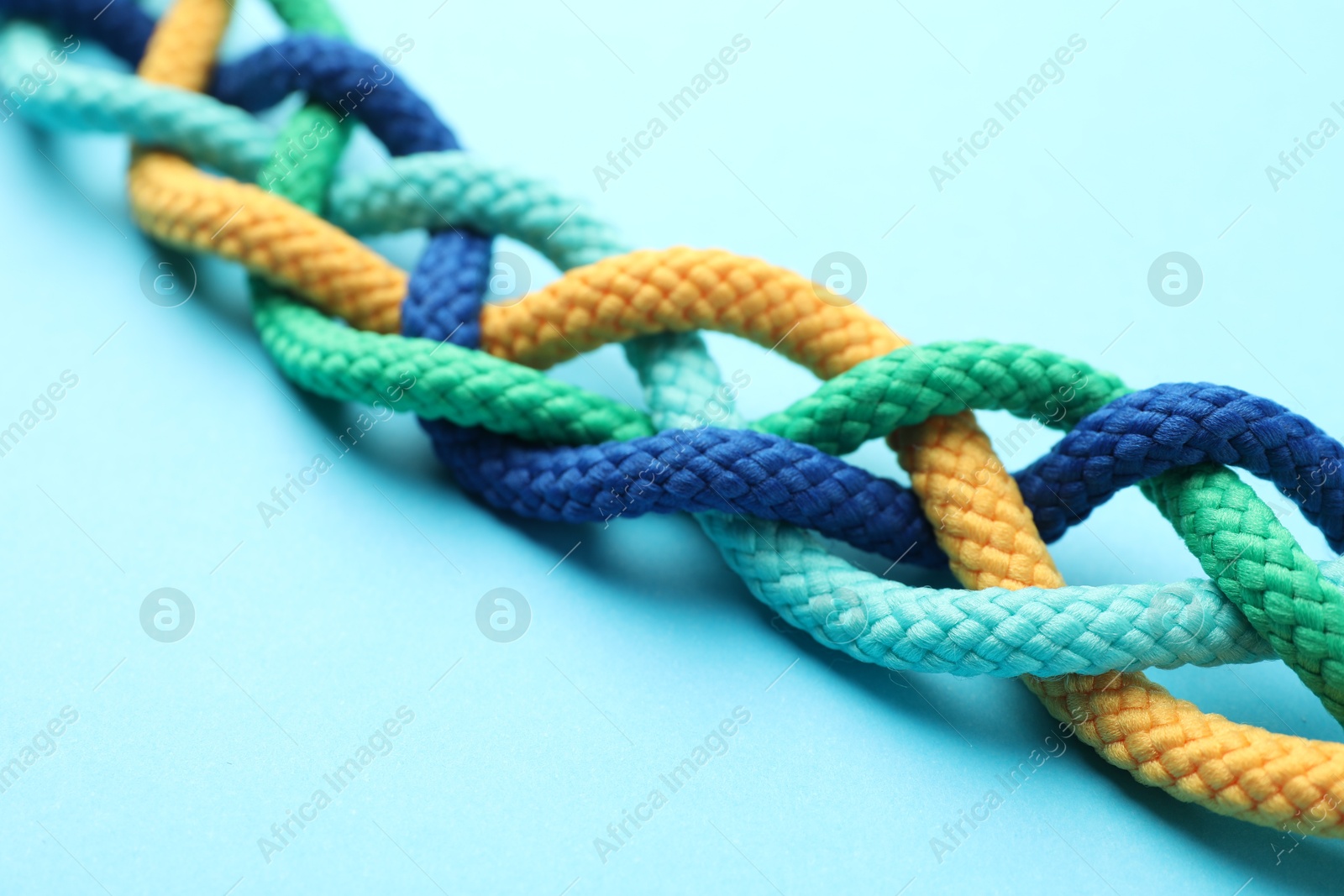 Photo of Braided colorful ropes on light blue background, closeup. Unity concept