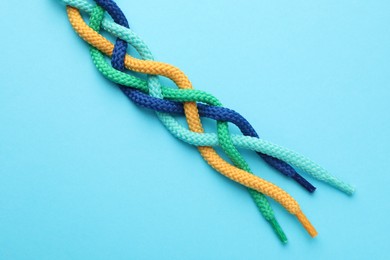 Photo of Braided colorful ropes on light blue background, top view. Unity concept