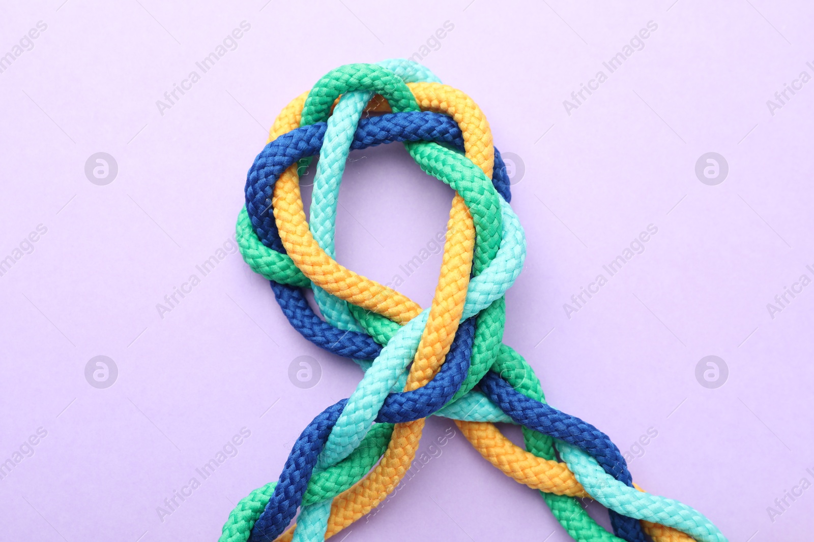 Photo of Braided colorful ropes on lilac background, top view. Unity concept